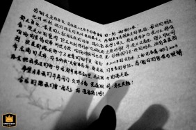 A black-and-white detail shot from Kaifeng, Henan, captures delicately held vow cards in the hands of the couple, focusing on the elegant script and the emotional significance of the promises exchanged.